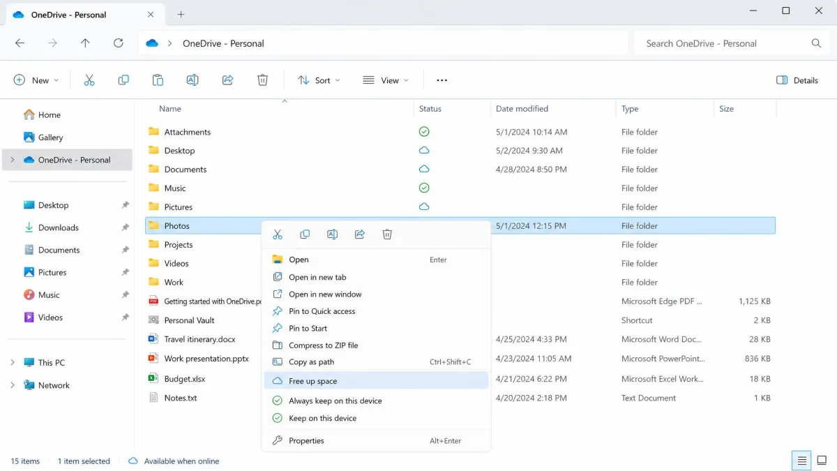 File Explorer OneDrive folder with the right-click menu open on a large Photos folder, showing the Free up space option highlighted and cloud placeholder status icons in the Status column.