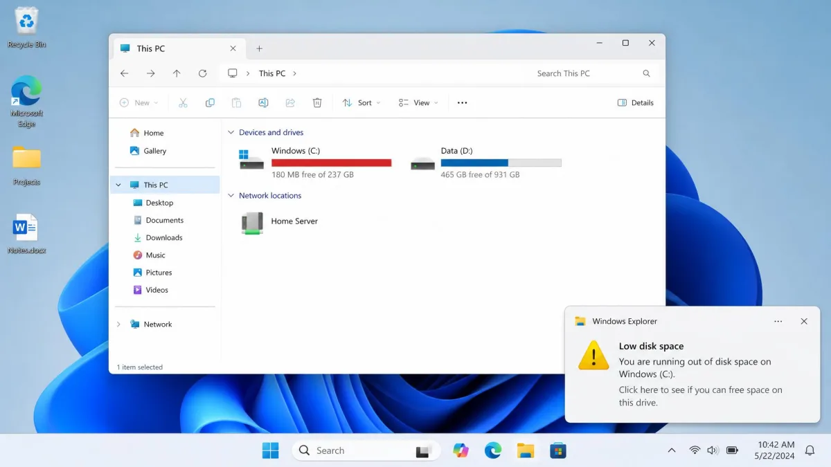 Windows 11 desktop showing the low disk space notification in the bottom-right corner, with the C: drive in File Explorer behind it displaying a red capacity bar and 180 MB free.