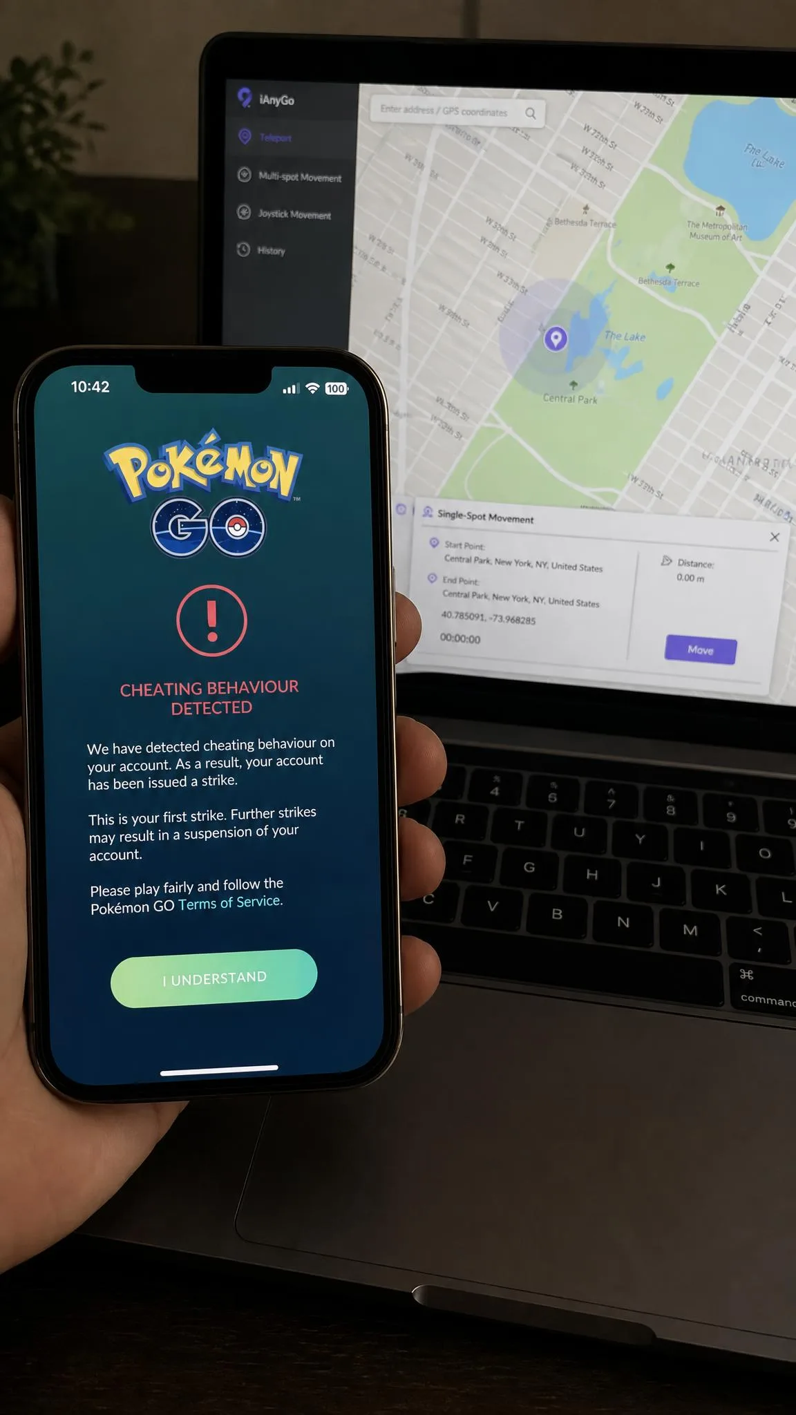 A Pokemon Go warning screen on an iPhone stating that cheating behaviour was detected, shown above a laptop running a location spoofing client.