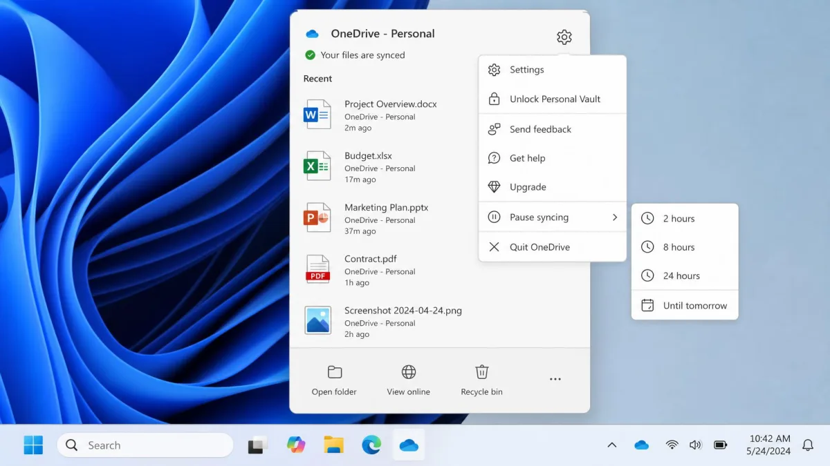 The OneDrive tray menu open on a laptop with the settings gear expanded and the Pause syncing submenu showing the 2, 8 and 24 hour options.