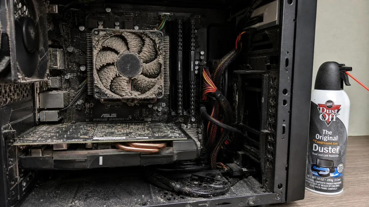 The inside of an open desktop PC case with a visibly dust-clogged CPU heatsink and fan, and a can of compressed air resting beside it.