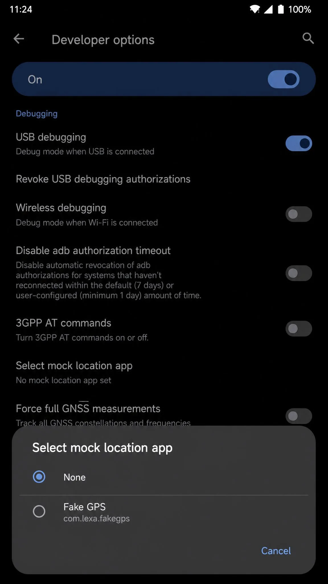 Android Developer options screen scrolled to the Debugging section with the Select mock location app dialog open and the None option selected.