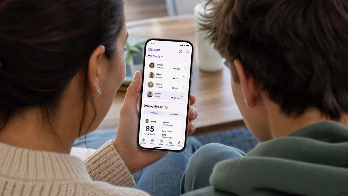A parent and a teenager looking at the Life360 Circle screen together on a phone, with the member list and the driving report tab visible.