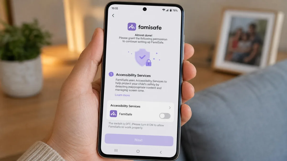 An Android phone during FamiSafe setup showing the Accessibility Services permission prompt with the FamiSafe toggle switched off and a parent's hand holding the device.