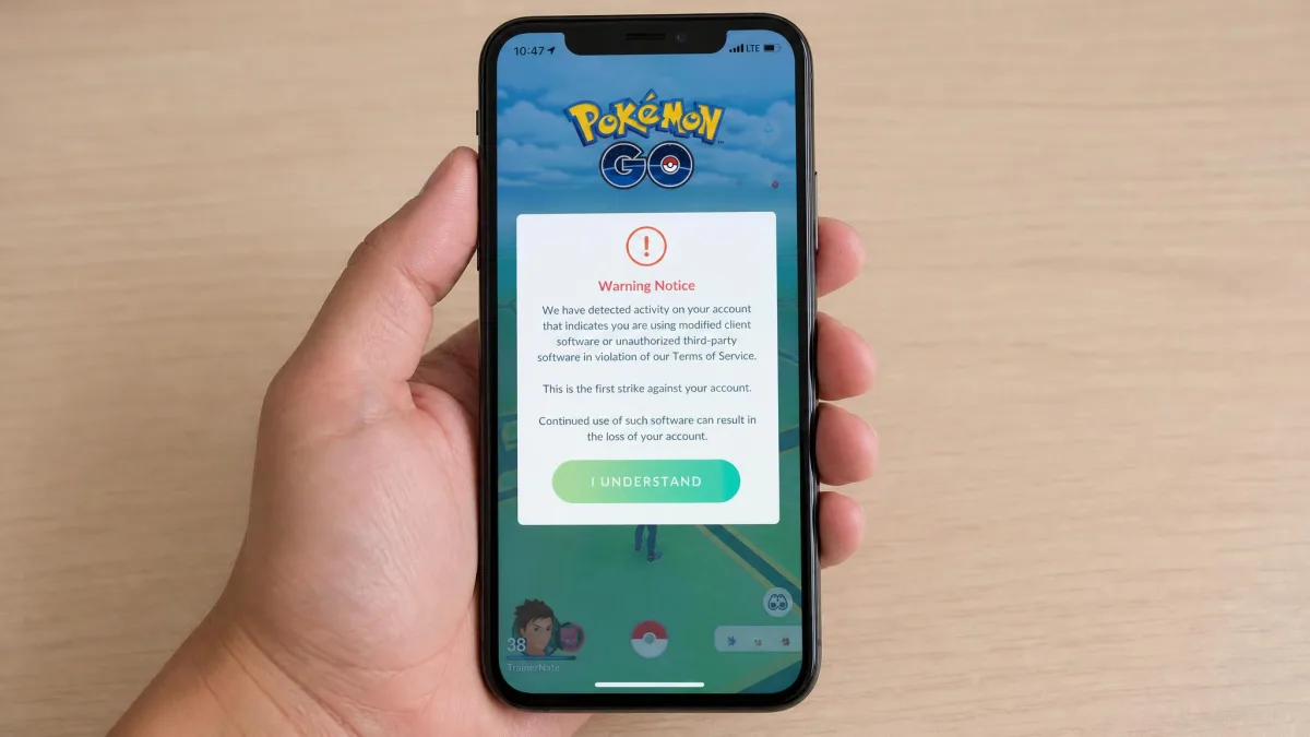 A smartphone showing Pokemon GO's in-game warning screen about third-party software use, held in one hand against a plain desk background.
